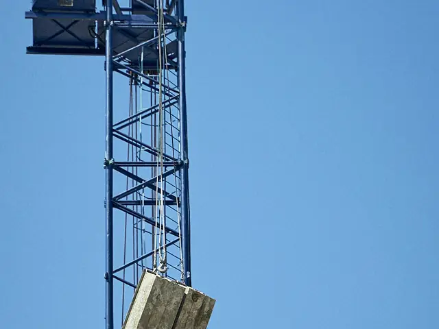 A construction tower crane lifting a concrete load against a clear blue sky